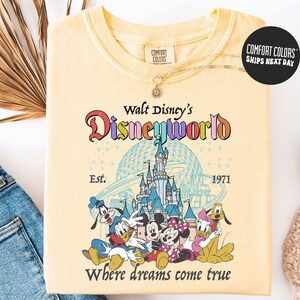 A yellow t-shirt with a Disney World logo and characters printed on it, along with a necklace and a pair of jeans.