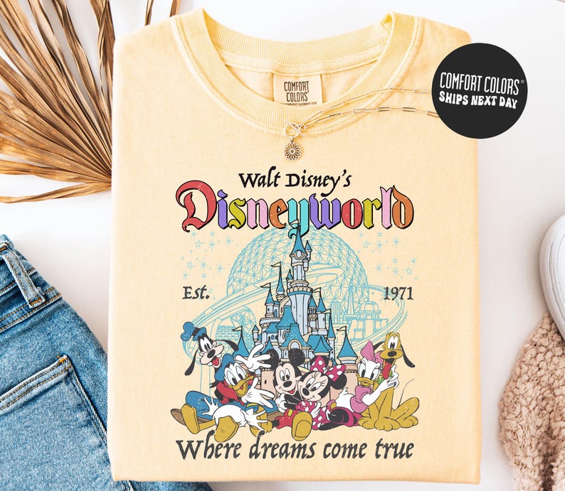 A yellow t-shirt with a Disney World logo and characters printed on it, along with a necklace and a pair of jeans.