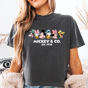 A woman wearing a gray t-shirt with a graphic of Mickey Mouse and Minnie Mouse, along with the text "MICKEY & CO. EST. 1978".