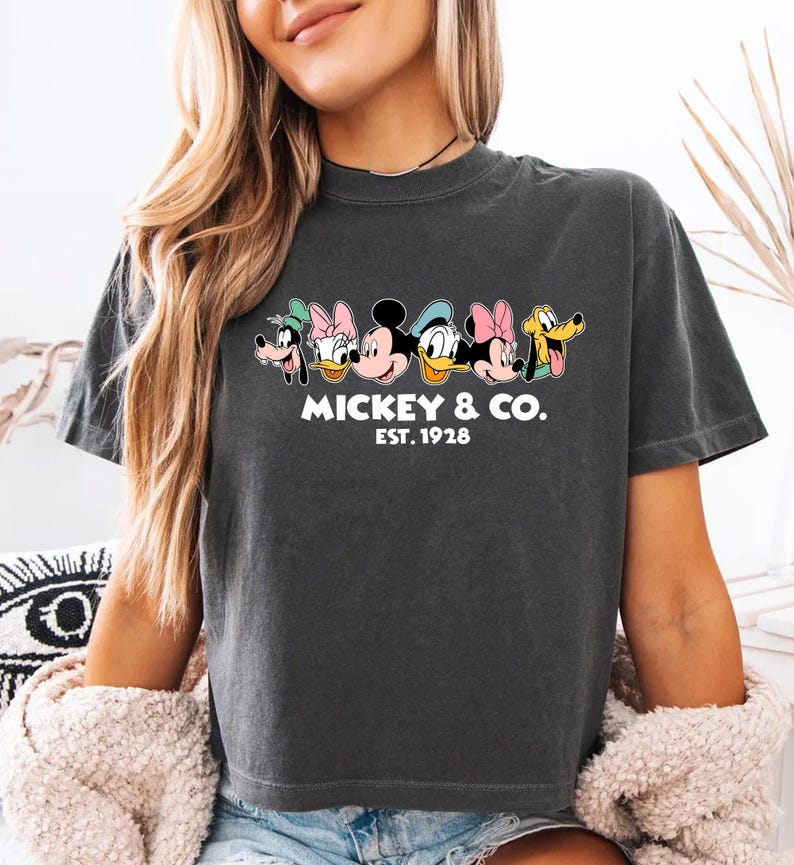 A woman wearing a gray t-shirt with a graphic of Mickey Mouse and Minnie Mouse, along with the text "MICKEY & CO. EST. 1978".