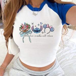 A person wearing a white and blue crop top with a graphic design featuring characters from the Disney movie Lilo and Stitch.
