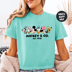A woman wearing a turquoise t-shirt with a graphic of Disney characters and text below them.