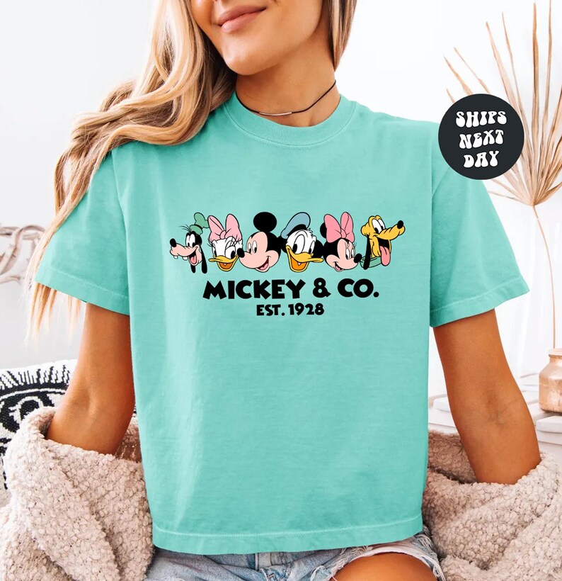 A woman wearing a turquoise t-shirt with a graphic of Disney characters and text below them.