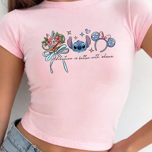 A woman wearing a pink t-shirt with a graphic design featuring a character from the Disney movie Lilo and Stitch, along with other Disney-themed elements.