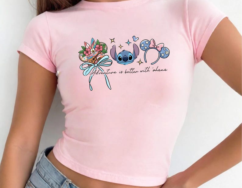 A woman wearing a pink t-shirt with a graphic design featuring a character from the Disney movie Lilo and Stitch, along with other Disney-themed elements.