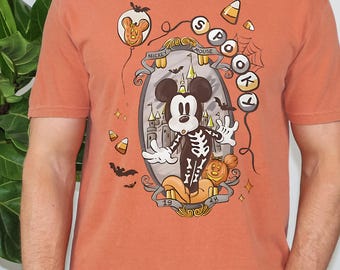 May include: Orange t-shirt featuring a Halloween-themed Mickey Mouse design. Mickey is dressed as a skeleton, with a castle, bats, and candy corn accents. The shirt has the words "SPOTLIGHT" and "MICKEY MOUSE" on it.