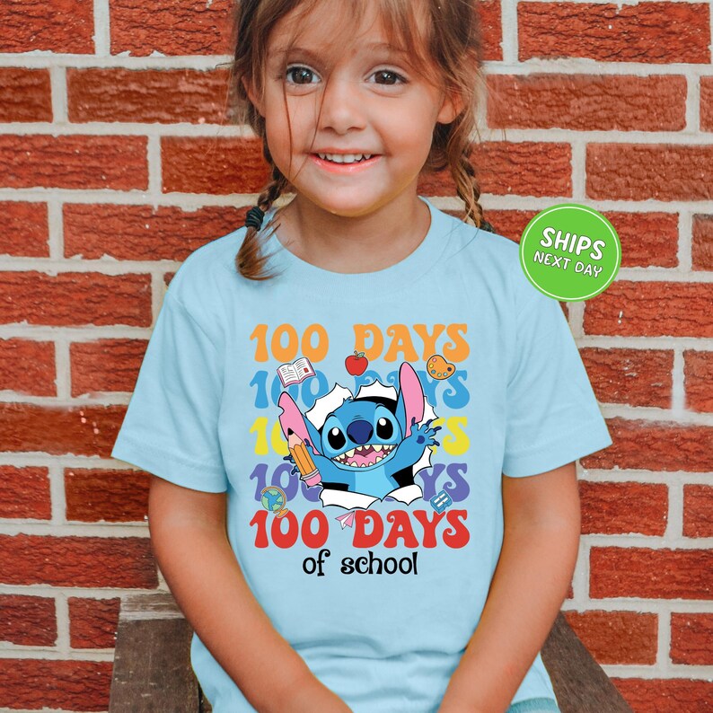 A young girl wearing a light blue t-shirt with a colorful graphic design celebrating 100 days of school.