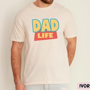 A man wearing a white t-shirt with the text "DAD LIFE" printed on it.
