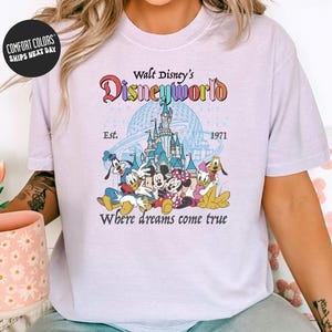 A woman wearing a white t-shirt with a Disney World logo and text, sitting on a couch with a coffee mug in front of her.