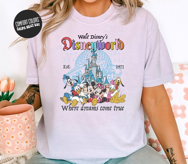 A woman wearing a white t-shirt with a Disney World logo and text, sitting on a couch with a coffee mug in front of her.