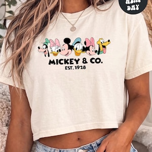 A woman wearing a white crop top with a graphic of Mickey Mouse and Donald Duck, along with the text "Mickey & Co. EST. 1928".