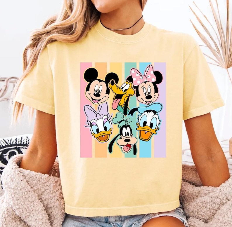 A yellow t-shirt with a colorful graphic of Disney characters such as Minnie Mouse, Mickey Mouse, Donald Duck, Goofy, and Pluto.