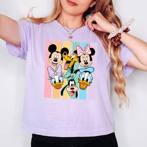 A woman wearing a purple t-shirt with a graphic of Disney characters Mickey Mouse, Minnie Mouse, Goofy, Donald Duck, and Pluto.