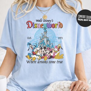 A woman wearing a light blue t-shirt with a Disney World logo and text, including the iconic Disney characters Mickey Mouse, Minnie Mouse, Donald Duck, and Goofy.