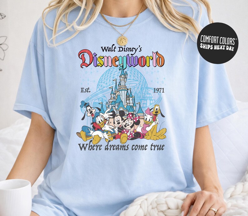 A woman wearing a light blue t-shirt with a Disney World logo and text, including the iconic Disney characters Mickey Mouse, Minnie Mouse, Donald Duck, and Goofy.