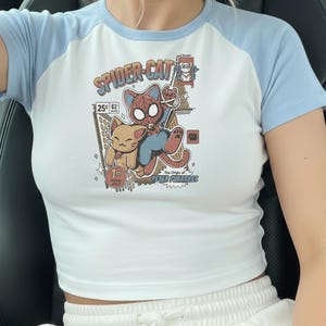 a person wearing a white crop top with a Spider-Cat graphic printed on it.