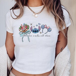 A woman wearing a white t-shirt with a graphic design featuring a blue character and various Disney-themed elements.