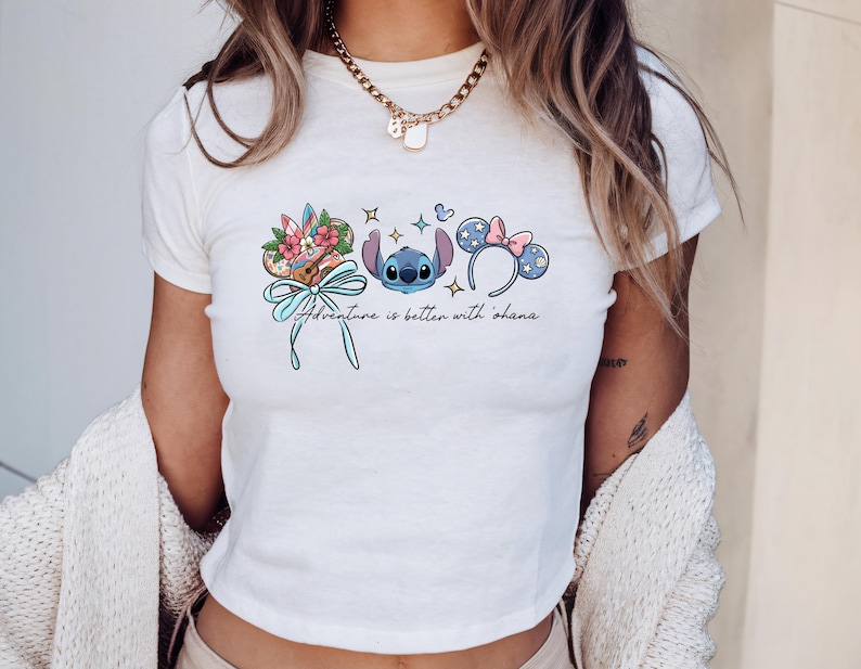 A woman wearing a white t-shirt with a graphic design featuring a blue character and various Disney-themed elements.