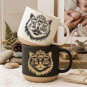 May include: Two ceramic mugs stacked on top of each other. The top mug is white with a black cat graphic wearing sunglasses and a crown, with the text "THIS IS AN OUTRAGE!". The bottom mug is black with a gold cat graphic and the same text.