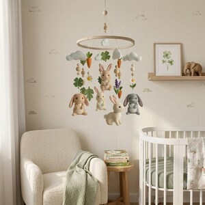 May include: A nursery mobile featuring a circular wooden frame with hanging felt elements including four rabbits in shades of brown, gray, and cream, white clouds, orange carrots, green clover leaves, and white daisy flowers suspended by thin strings.