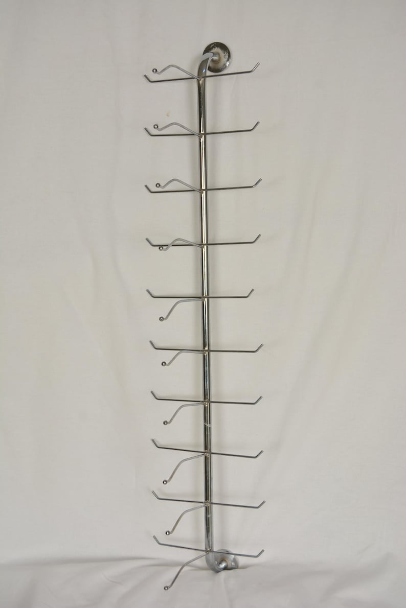 Pode incluir: Um expositor vertical de metal cromado com uma haste central e dez pares de bra&ccedil;os horizontais que se estendem para fora. Cada bra&ccedil;o possui uma pequena ponta esf&eacute;rica na extremidade, projetado para organizar e exibir v&aacute;rios objetos.