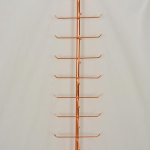 Pode incluir: Um expositor vertical de metal na cor cobre, apresentando uma haste central com dez bra&ccedil;os horizontais que se estendem de cada lado. Cada bra&ccedil;o termina num pequeno gancho curvado para cima. A estrutura inclui placas de montagem circulares.