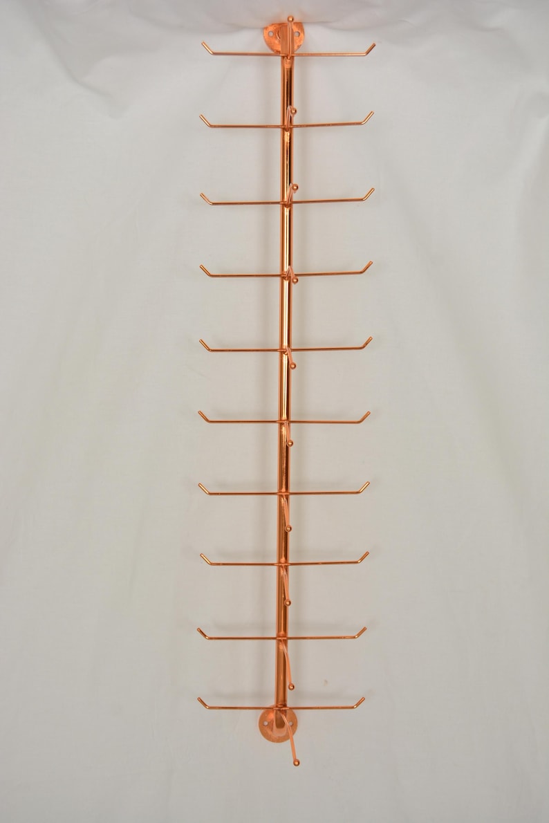 Pode incluir: Um expositor vertical de metal na cor cobre, apresentando uma haste central com dez bra&ccedil;os horizontais que se estendem de cada lado. Cada bra&ccedil;o termina num pequeno gancho curvado para cima. A estrutura inclui placas de montagem circulares.