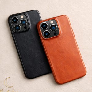 Könnte beinhalten: Zwei Leder-Handyhüllen, eine schwarze und eine orangefarbene, werden gezeigt. Die Hüllen haben eine strukturierte Oberfläche und einen Kameraausschnitt mit mehreren Linsen. Die Hüllen sind abgewinkelt, wodurch ihr Design und ihre Textur hervorgehoben werden.