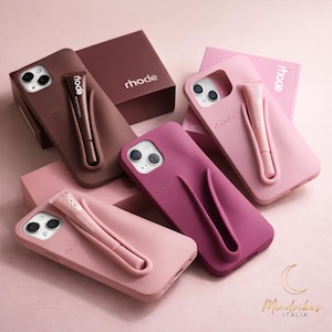 Op de afbeelding: Een verzameling telefoonhoesjes in verschillende tinten roze en bruin, elk met een bijpassend lipproduct. De hoesjes hebben een strak ontwerp met de merknaam "rhode". De afbeelding bevat ook dozen met de merknaam.