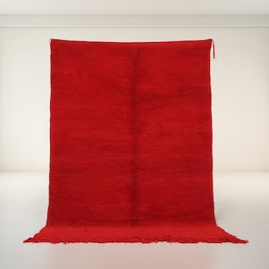 A large, vibrant red rug is displayed in a minimalist, white-walled room with two windows.