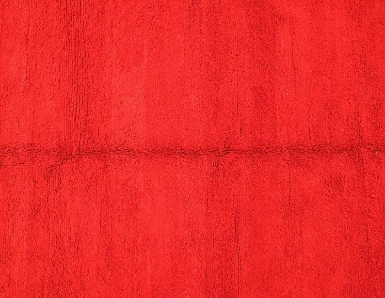 The image is a close-up of a red fabric or surface, with a textured and slightly wrinkled appearance.