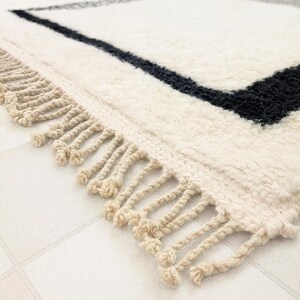 A close-up view of a white and black rug with fringe, placed on a tiled floor.