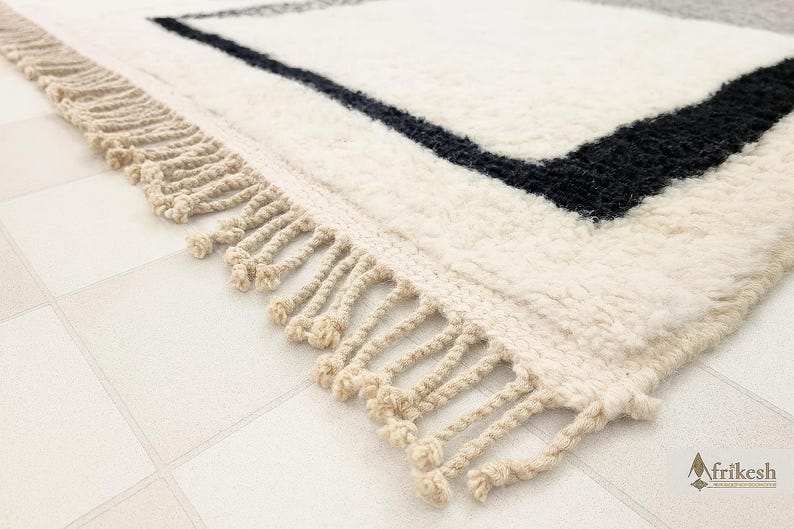 A close-up view of a white and black rug with fringe, placed on a tiled floor.