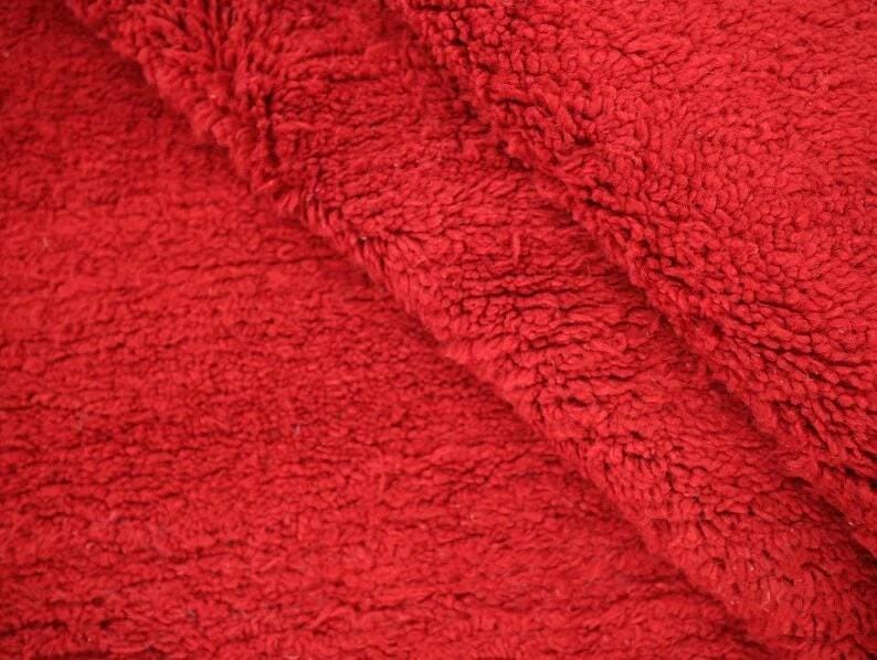 A close-up view of a red, fluffy fabric, possibly a blanket or towel, with a textured and soft appearance.