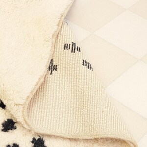 a close-up view of a beige rug with black spots, placed on a white checkered floor.