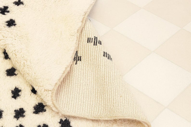 a close-up view of a beige rug with black spots, placed on a white checkered floor.