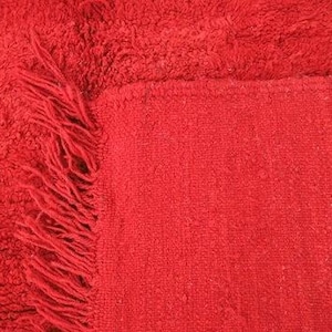 A close-up image of a red fabric with a fringed edge, likely a piece of clothing or textile.