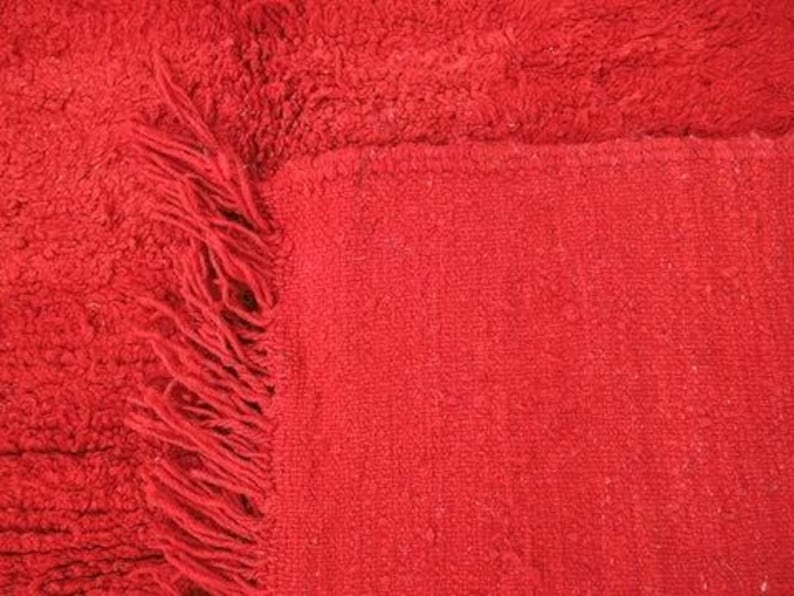 A close-up image of a red fabric with a fringed edge, likely a piece of clothing or textile.