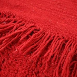A close-up view of a red, textured fabric with fringed edges, creating a soft and cozy appearance.