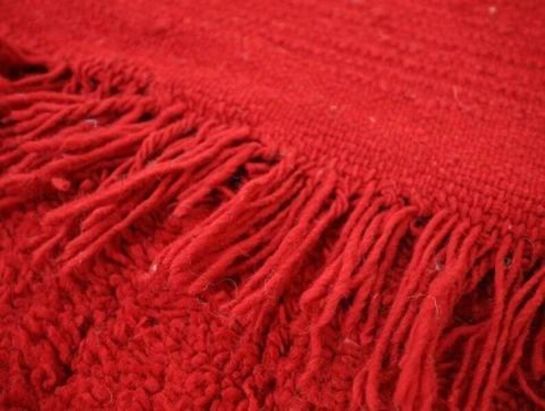 A close-up view of a red, textured fabric with fringed edges, creating a soft and cozy appearance.