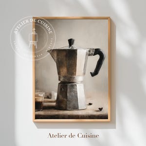 May include: A framed print featuring a vintage-style illustration of a stovetop espresso maker. The metallic coffee pot has a black handle and lid. The print includes the text "Atelier de Cuisine" and a circular logo.