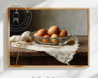 May include: A framed print featuring a still life of eggs in a clear glass bowl. The eggs are various shades of brown and are resting on a white cloth. The print is on a wooden table with the text "Atelier de Cuisine".