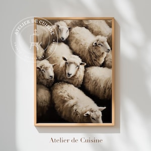 May include: A framed print showing a watercolour painting of a flock of sheep. The sheep are depicted in shades of white and beige, with a focus on their fluffy wool. The artwork is framed in a light brown wooden frame. The text "Atelier de Cuisine" is at the bottom.