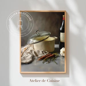 May include: A framed print featuring a still life of kitchen items. A cream-colored pot with a glass lid sits next to a bottle of wine, carrots, garlic, and herbs. The print has the text "Atelier de Cuisine" and a circular logo.