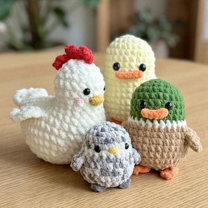 Könnte beinhalten: Vier handgefertigte Häkelfiguren von Tieren: ein weißes Huhn mit rotem Kamm, ein gelbes Entenküken, ein grauer Pinguin und eine grüne und braune Ente. Die Figuren stehen auf einer Holzoberfläche.