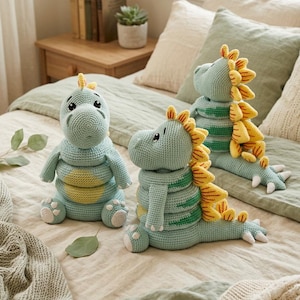 Puede incluir: Tres peluches de dinosaurio hechos a mano con ganchillo en tonos de azul, amarillo y verde. Los dinosaurios tienen detalles, incluyendo espinas, rayas y pequeñas garras blancas. Están colocados sobre una cama con una manta de tonos neutros.