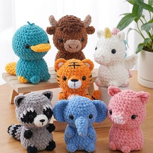 Könnte beinhalten: Eine Sammlung von sieben handgefertigten Häkeltier-Plüschtieren. Die Plüschtiere umfassen ein blaues Schnabeltier, einen braunen Bullen, einen orangefarbenen Tiger, ein weißes Einhorn, einen grauen Waschbären, einen blauen Elefanten und ein rosa Schwein. Jedes Plüschtier ist etwa 10-15 cm groß.