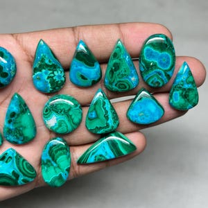 May include: A collection of polished gemstones in various shapes, including teardrops, ovals, and triangles. The stones display a striking combination of teal and deep green hues, with intricate patterns and swirls. The gemstones are held in a hand.