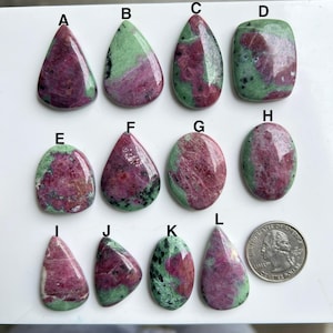 May include: A collection of polished ruby in zoisite gemstones in diverse shapes, such as teardrop, oval, and rectangular. The stones exhibit a blend of deep red and green colours. A US quarter is included for size reference.