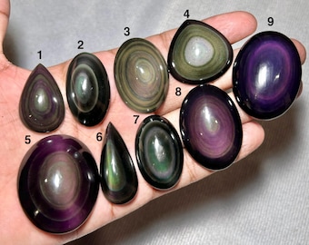 May include: Nine polished rainbow obsidian cabochons labeled one through nine. These smooth, oval and teardrop-shaped stones feature concentric bands of iridescent purple, green, and gold colors against a deep black background.